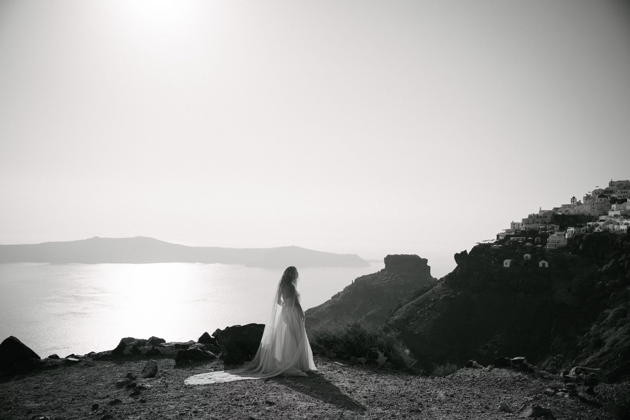 Black-and-white bridal portrait of Margi looking out across Santorini’s caldera