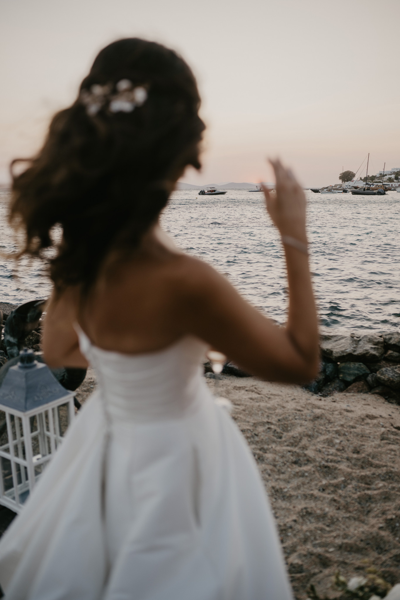 Martina in her wedding dress facing the Aegean with the Mykonos shoreline behind her.