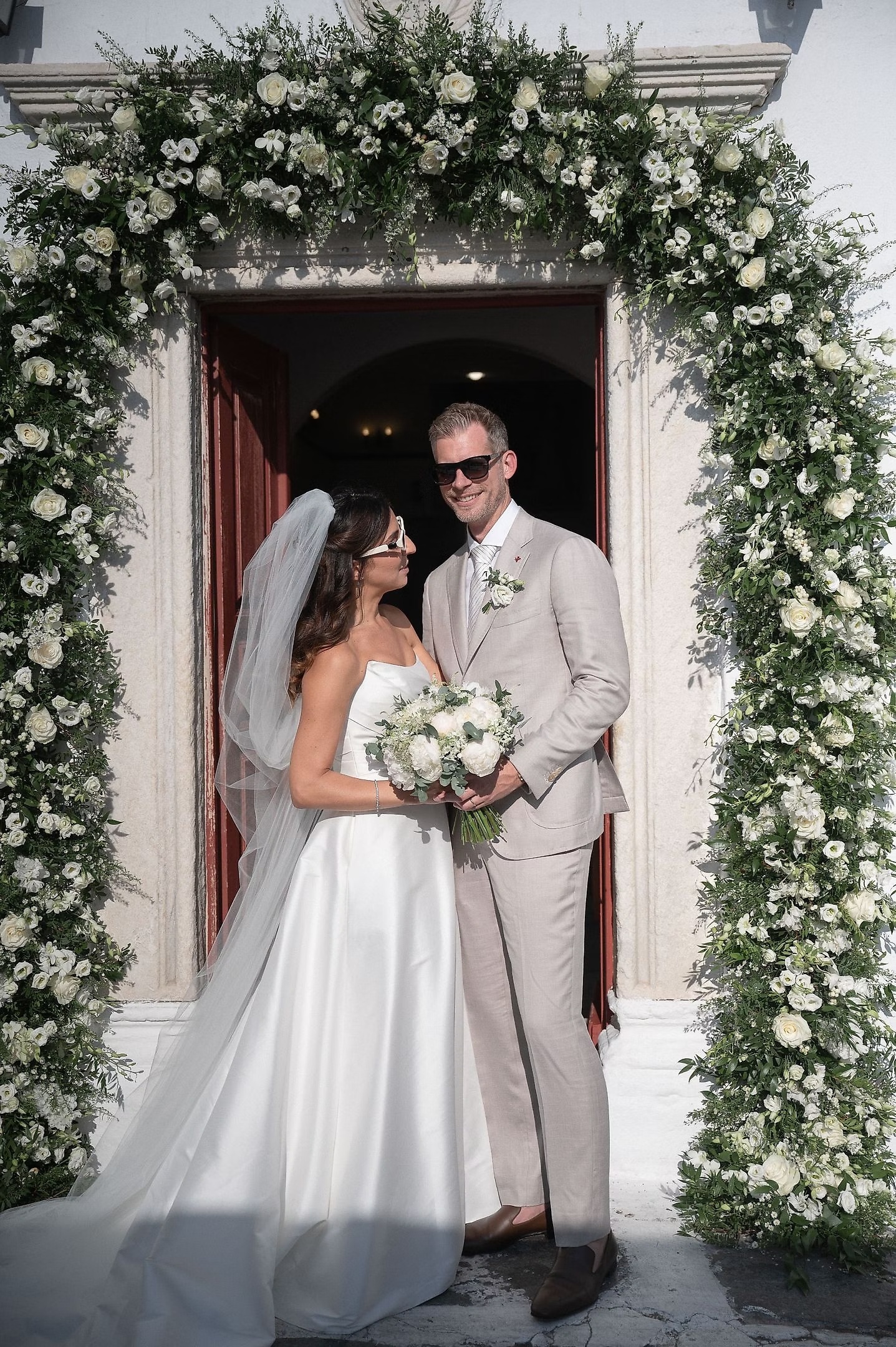 Martina and Justin sharing a moment beneath a white floral entrance in Mykonos