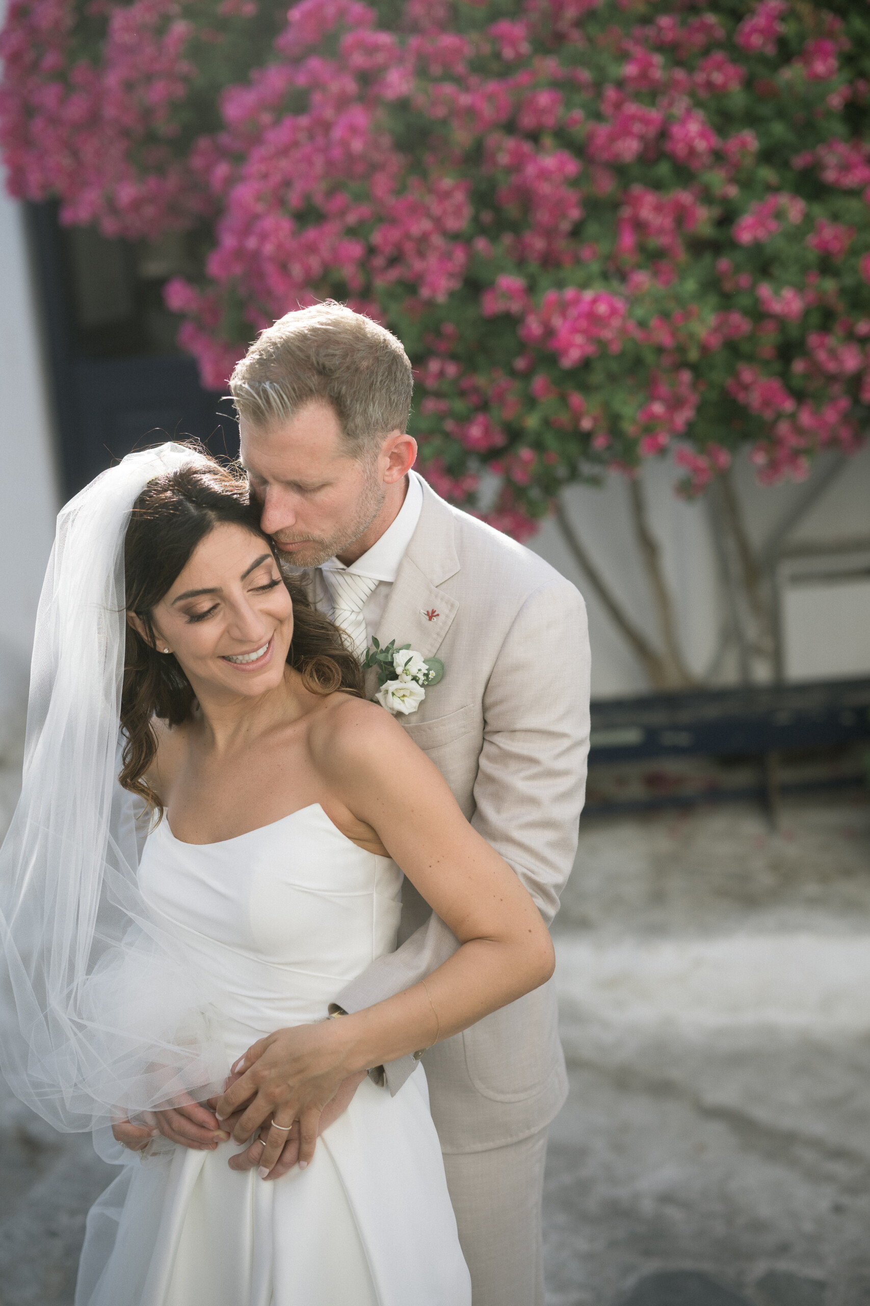Martina and Justin sharing a tender moment beneath pink bougainvillea during their Mykonos wedding.