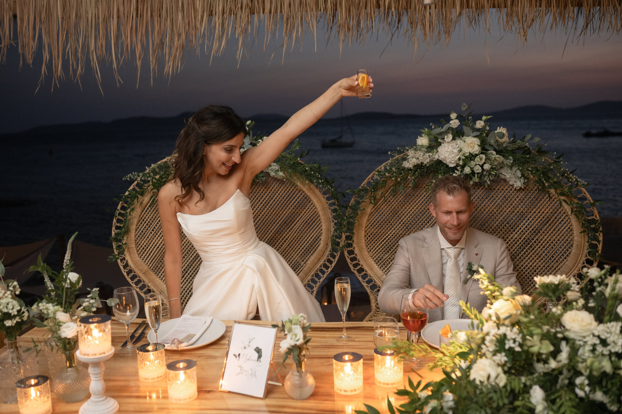 Martina and Justin raise a toast at their decorated wedding table by the sea.