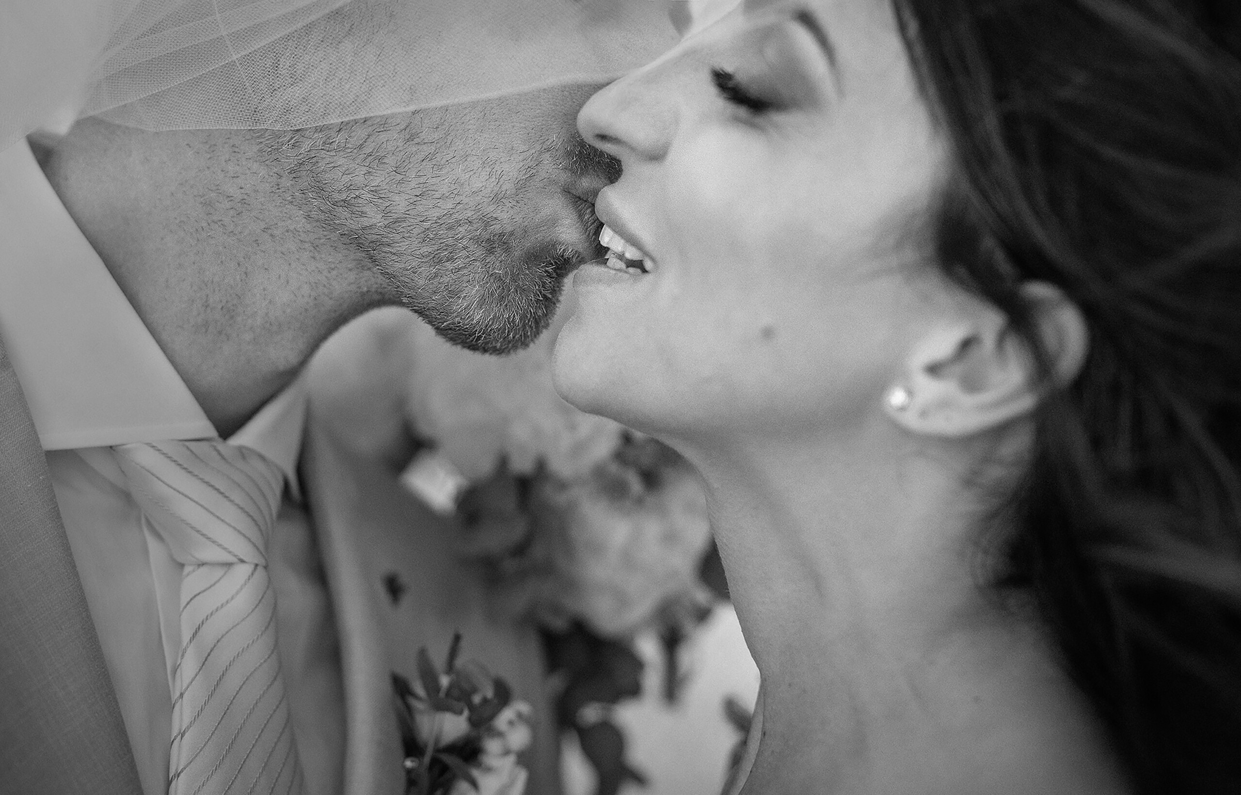 Martina and Justin sharing an intimate kiss beneath her veil in a black-and-white wedding portrait.