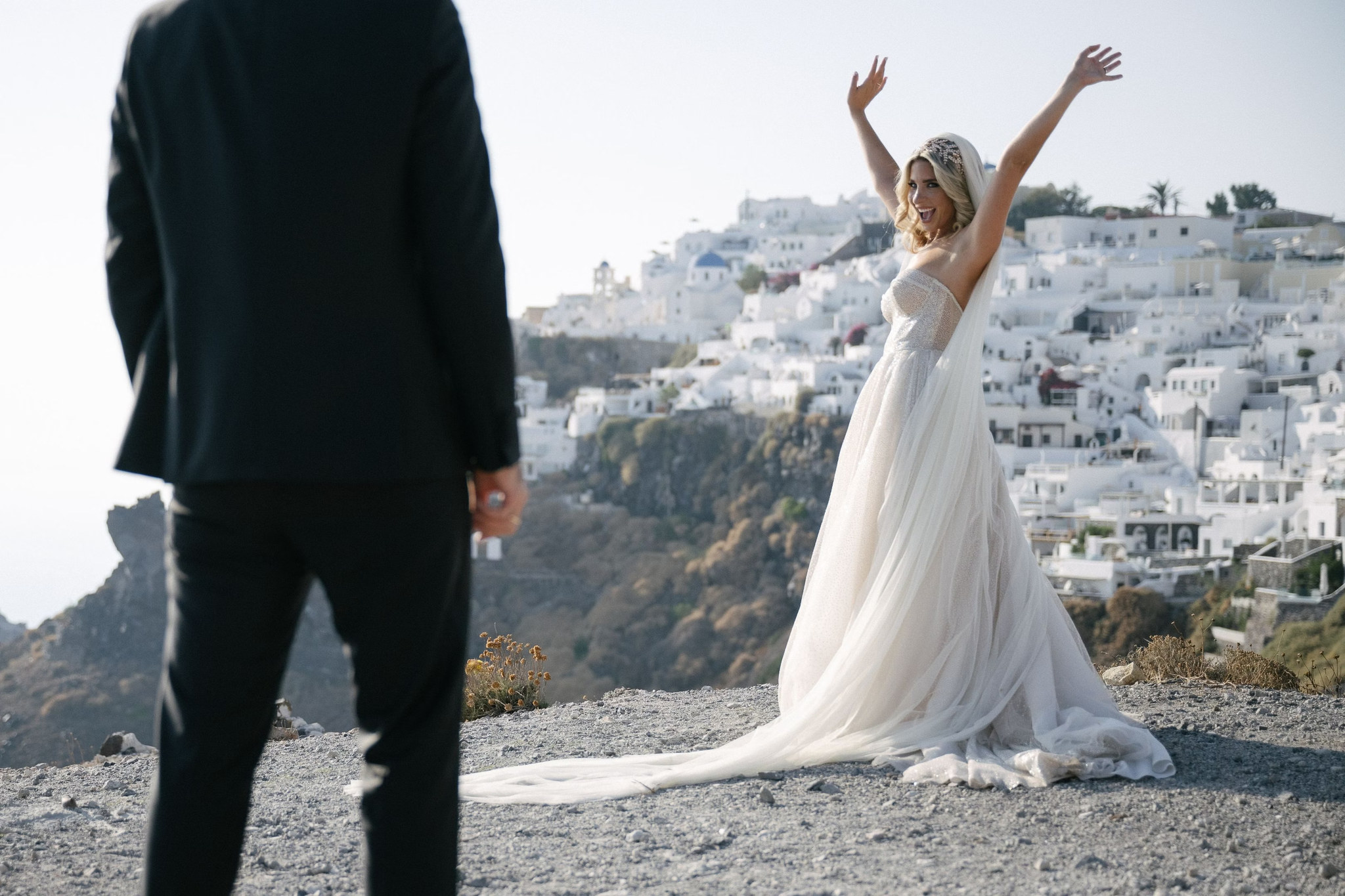 Margi celebrating in her wedding dress with Santorini’s whitewashed hillside buildings behind her